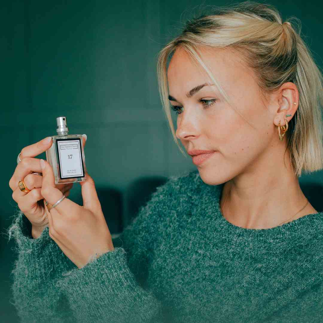 Image of a woman in a green jumper holding a perfume from The Essence Vault, Beyond Smelling Good: Why Do Women Wear Perfume